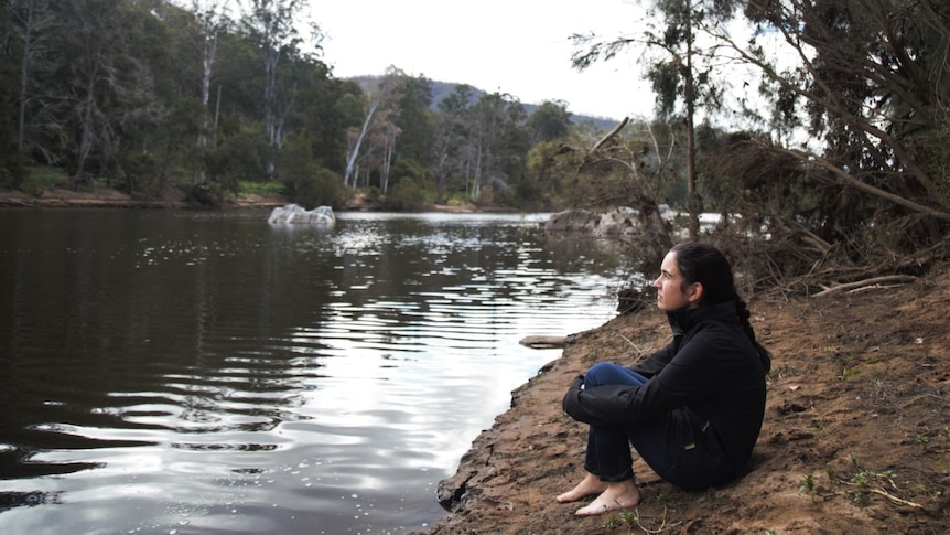 A woman sits beside a river.