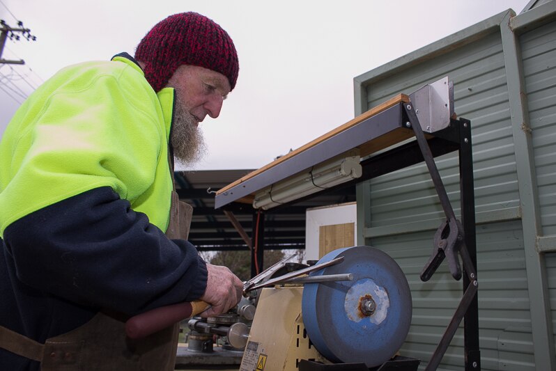 A man putting a pair of garden secateurs on a sharpening machine