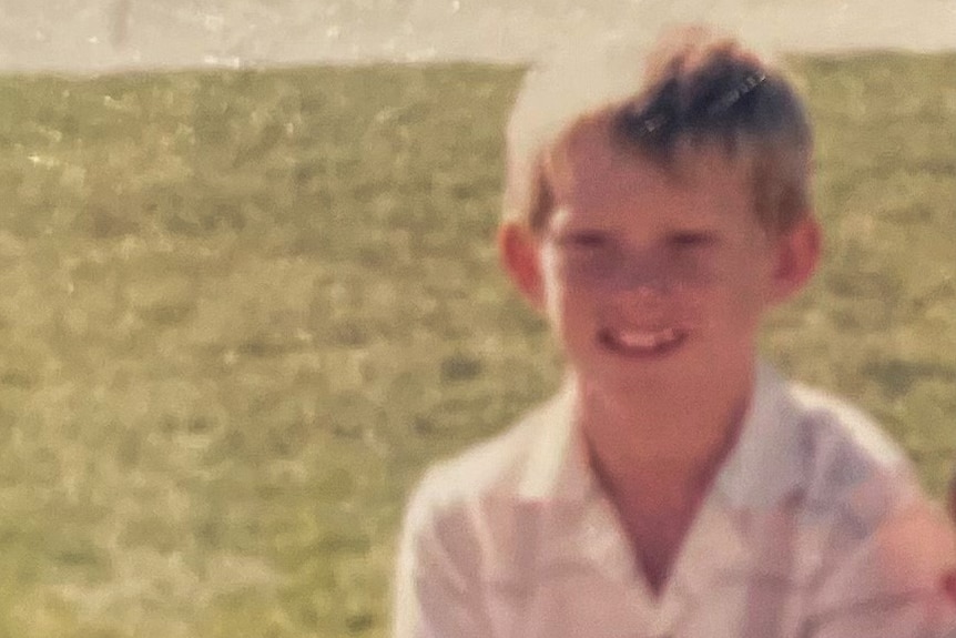 An old photo of a boy sitting down on a ledge in front of grass.