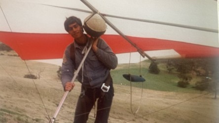 Um jovem está sob uma asa delta vermelha e branca. 