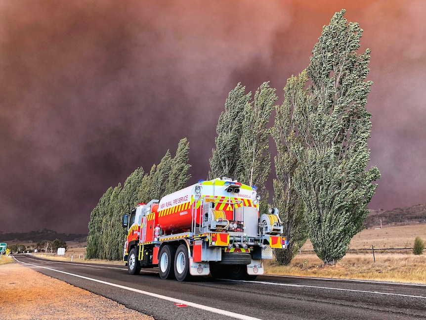 A firetruck on a road, with heavy smoke filling the sky.