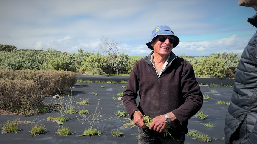 man is weeding wearing a dark jumper, sunglasses and a blue hat. He smiles at a man wearing a puffer jacket. 