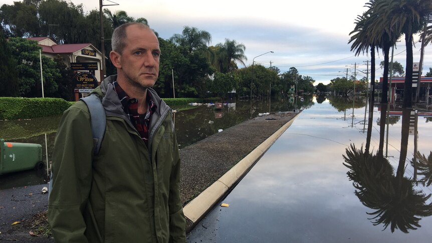 A man stands in front of a flooded road.