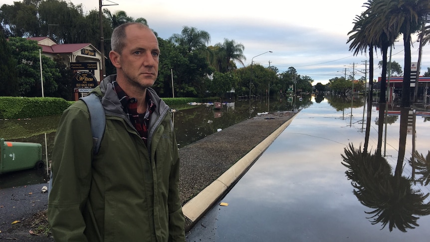 A man stands in front of a flooded road.