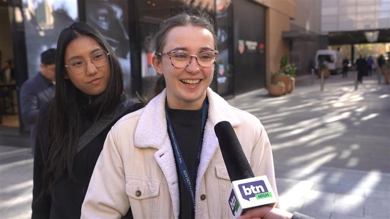 A young woman with glasses smiles and speaks into a BTN High microphone.