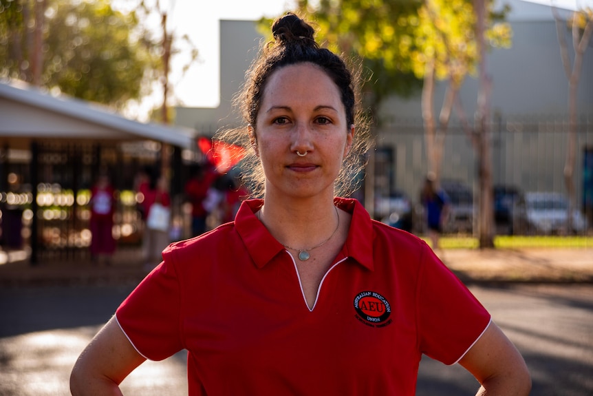 A woman wearing a red shirt looking directly at the camera in front of a park
