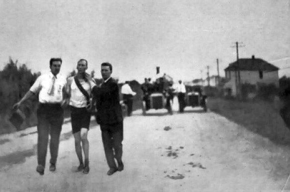 A black and white photo of two men holding up a runner on a road