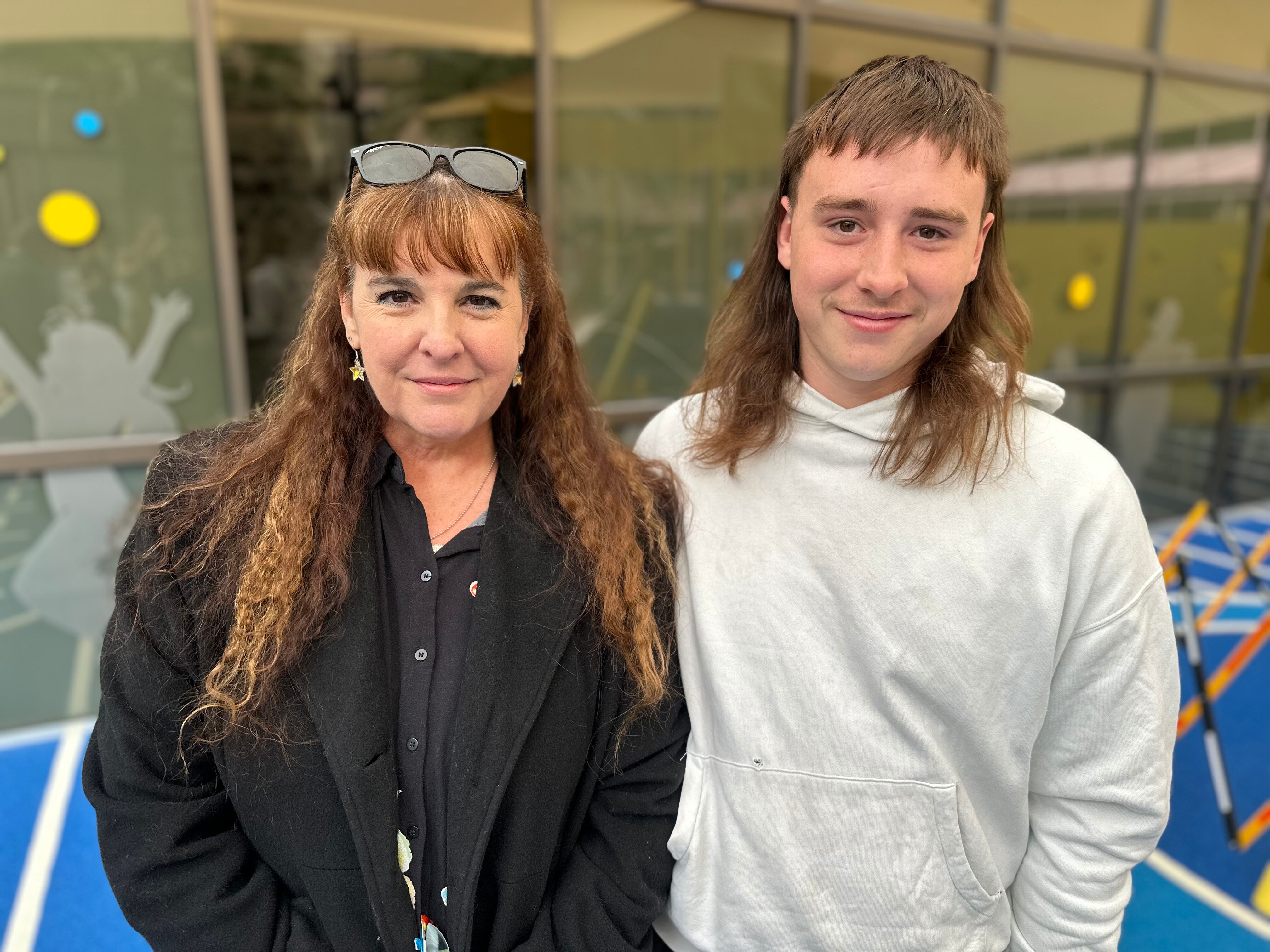A mother and son stand side by side and smile at the camera