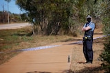 A masked police officer with his arms folded, police tape across a footpath