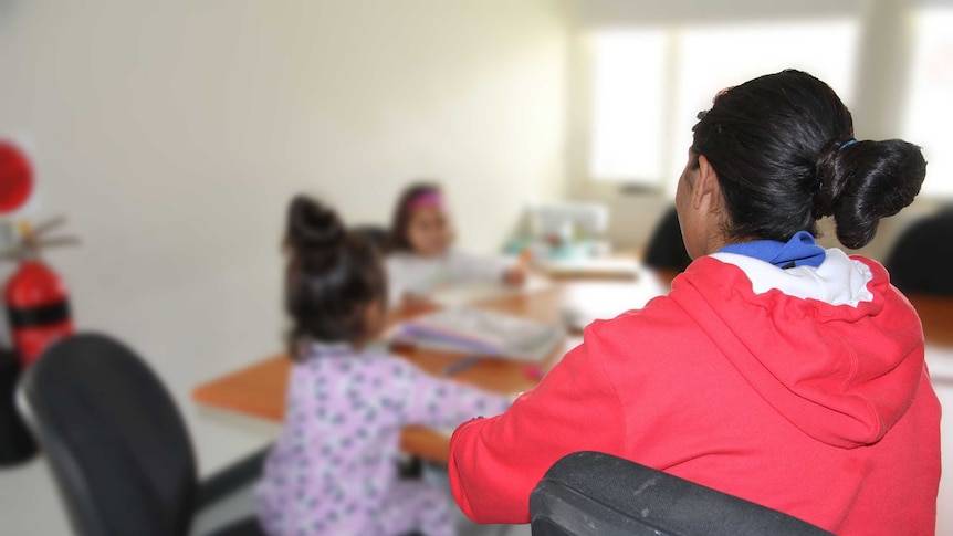 Broken Hill woman Delenna King sits with her back to the camera and her face obscured, with two children at a table, blurred out