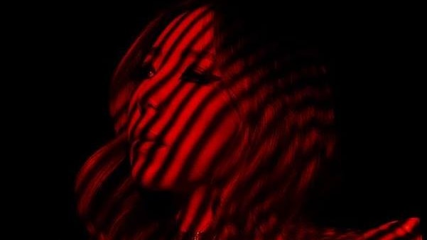 tokimonsta standing in shadows with red light cast across her face