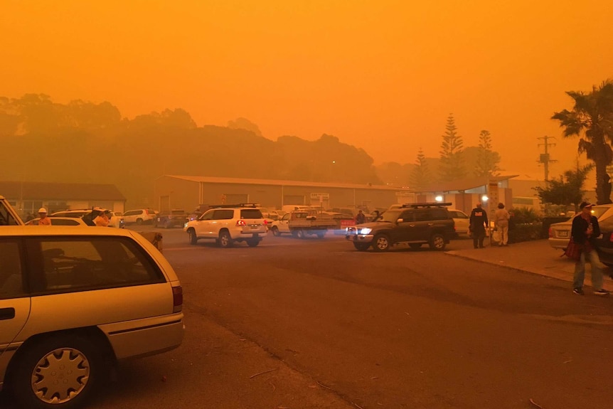 Cars leaving a carpark at Eden, New South Wales where the sky is orange.