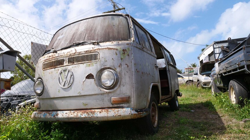 A rusty kombi van sits in a caryard.