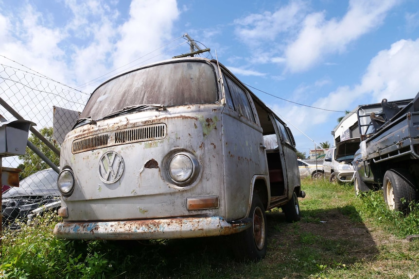 A rusty kombi van sits in a car yard.