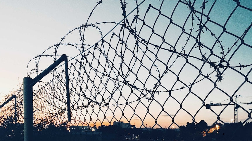 Wire on top of a wire fence as the sun sets behind it