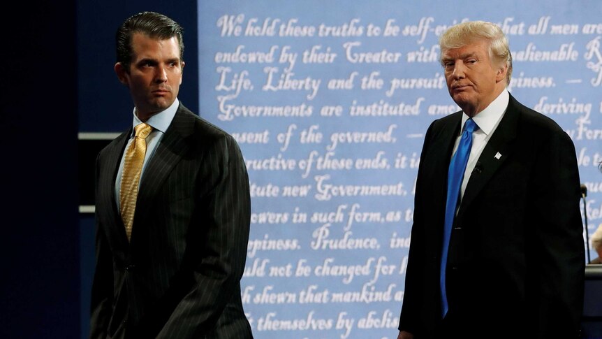 Donald Trump Jr and Donald Trump walk off a stage, backlit with the Declaration of Independence, with grim expressions