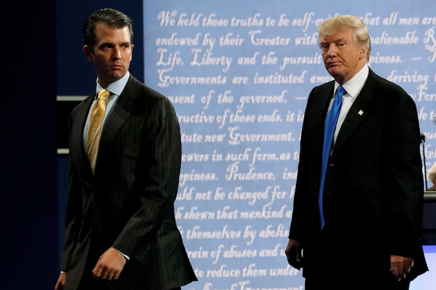 Donald Trump Jr and Donald Trump walk off a stage, backlit with the Declaration of Independence, with grim expressions