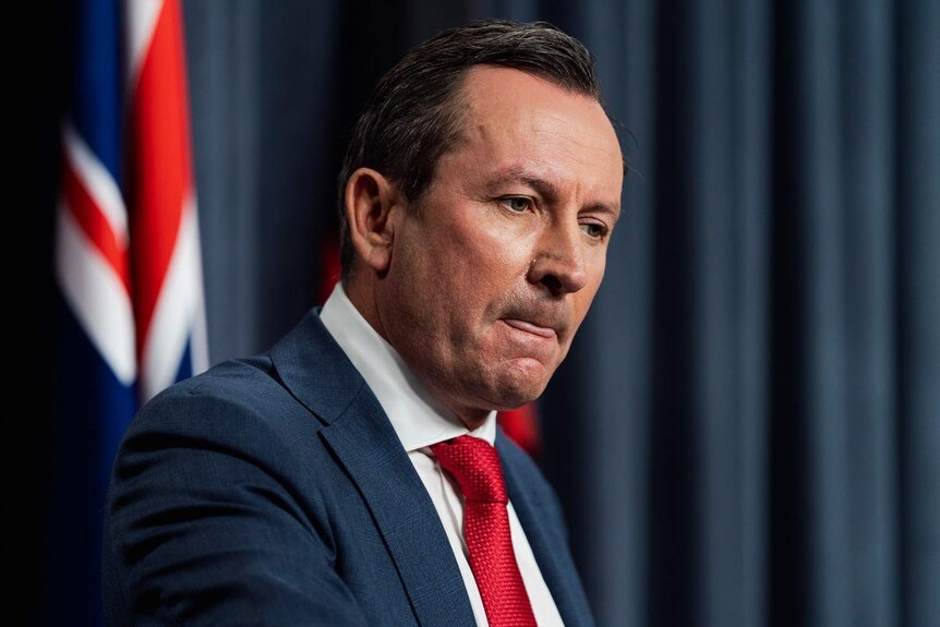 A close up of Mark McGowan speaking at a podium in front of Australian flags and a blue curtain.