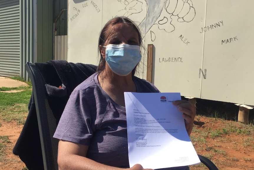 An Indigenous woman wearing a mask, holding up a piece of paper proving she's clear of COVID.