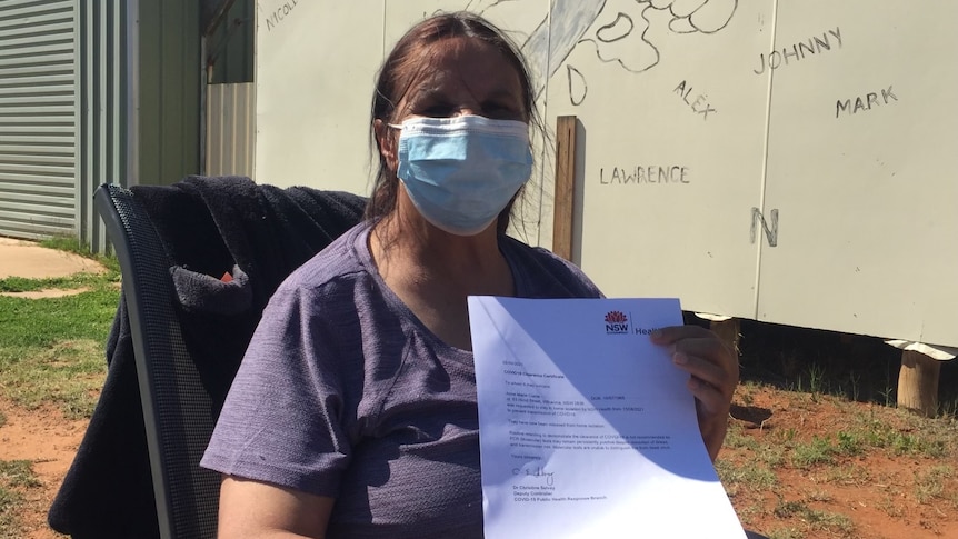 An Indigenous woman wearing a mask, holding up a piece of paper proving she's clear of COVID.