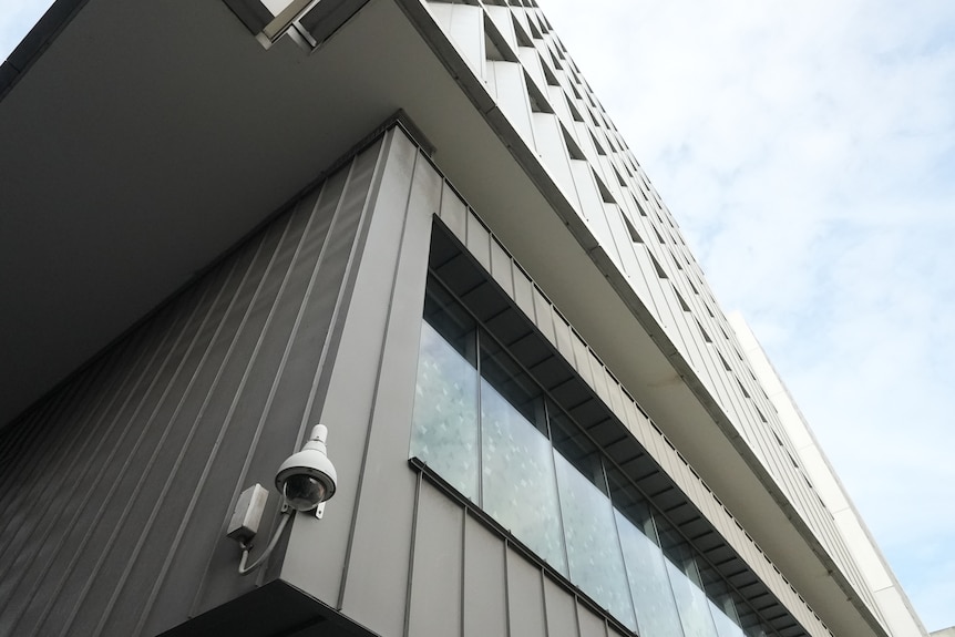 A university building shot from below. A security camera is mounted on the corner of the building.