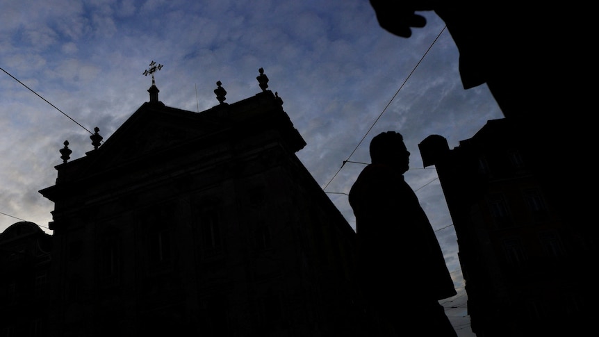 The silhouette of a church and a person walking by stands out against the evening sky