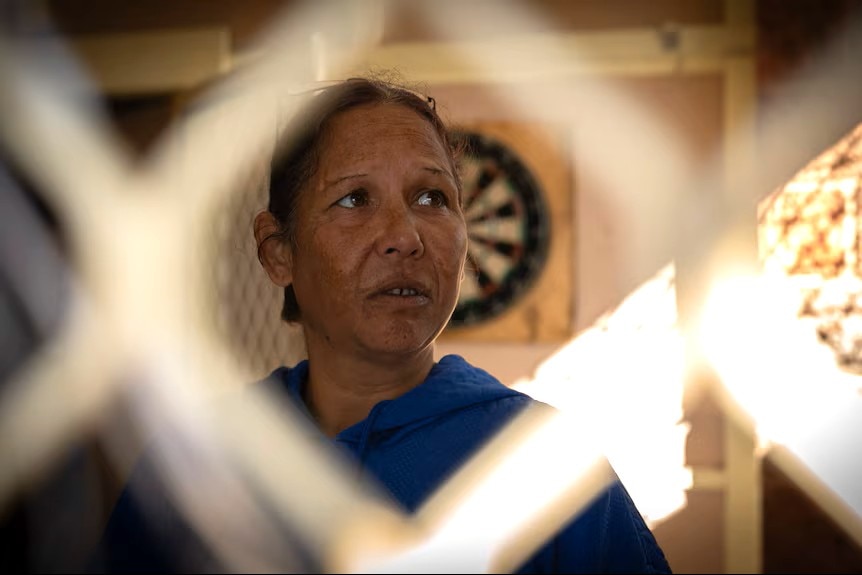 A woman stands behind a screen door.