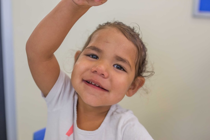 A young girl smiles and holds her hand above her head.