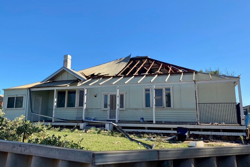 A weatherboard house with its roof ripped off.