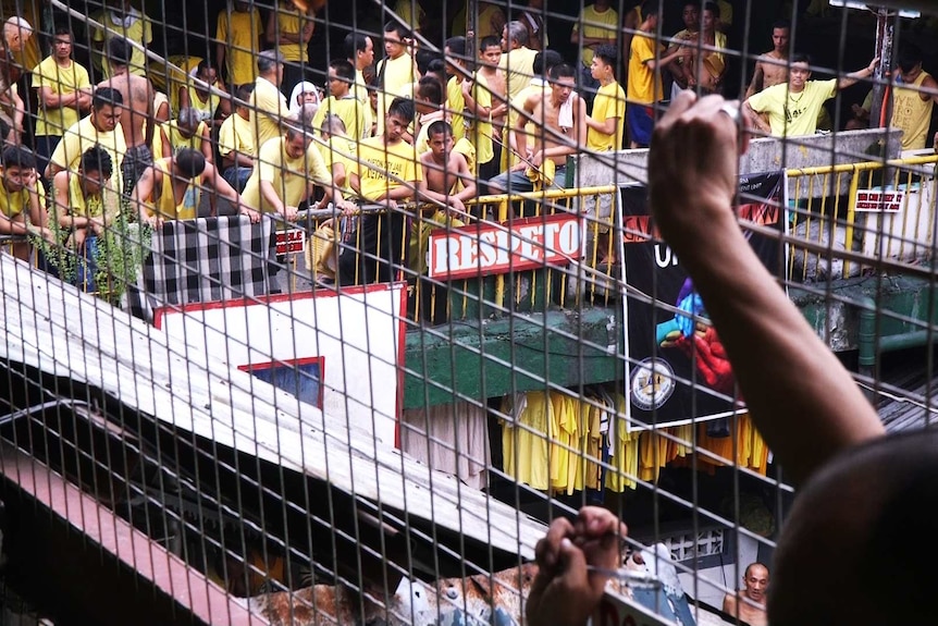 A crowded upper level of Quezon City Jail, seen through the wire cage of a stairwell.