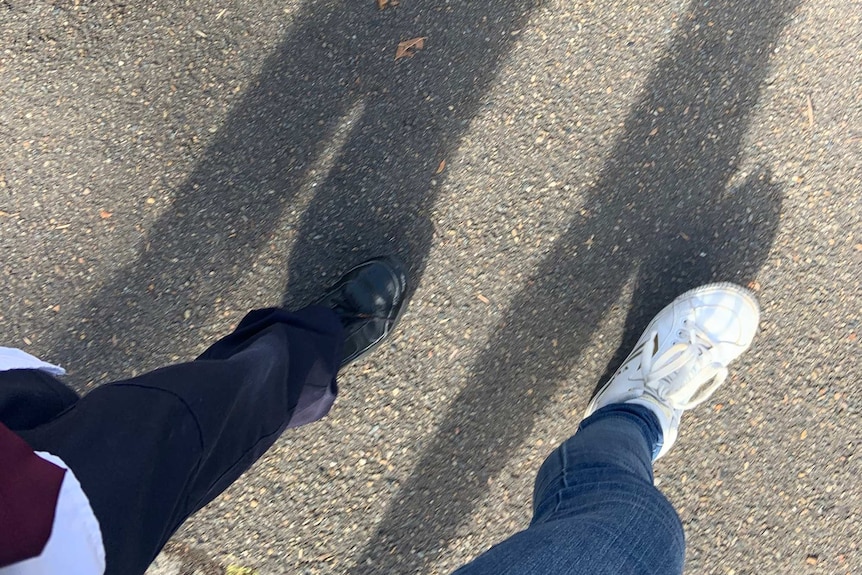 A school child and a parent walk on a footpath with a shadow in front of them