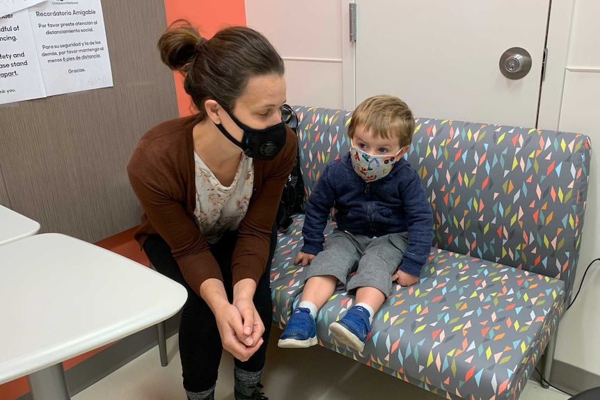 Little boy and woman sitting on couch in doctor's room wearing masks.