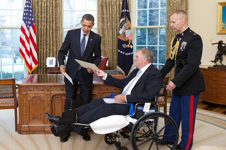 Barack Obama and Kim Beazley, who is in a wheel chair, hand eachother folders