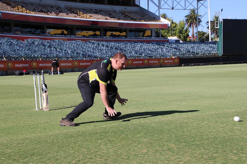 Blind cricket player Ryan Honschooten crouches down as prepares to grab the ball.
