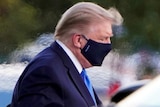 Donald Trump wears a mask and looks down.