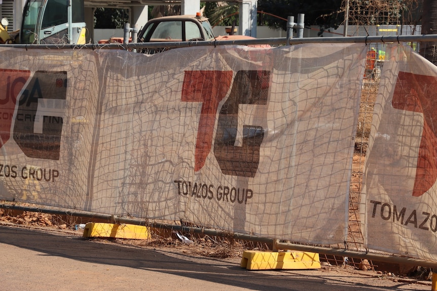 A banner with the words "Tomazos Group" attached to some construction site fencing.