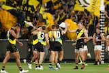 A number of Richmond players celebrate together. Behind them, yellow and black flags and banners are waving