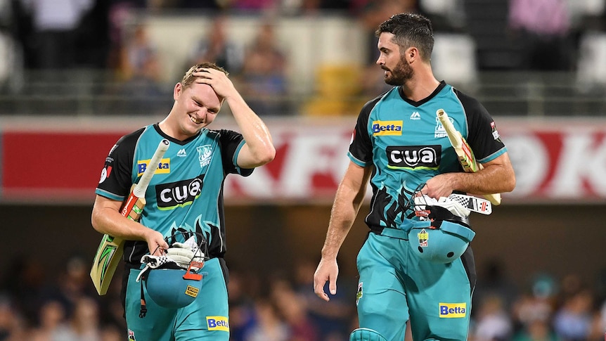 Two cricketers walk off the field, one rubbing his head after winning a Big Bash game.