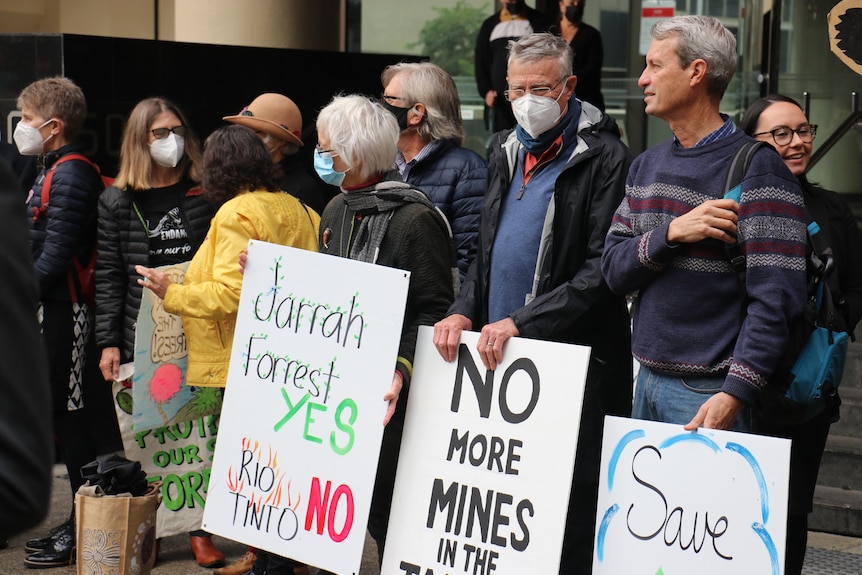 Protestors stand outside a building holding signs