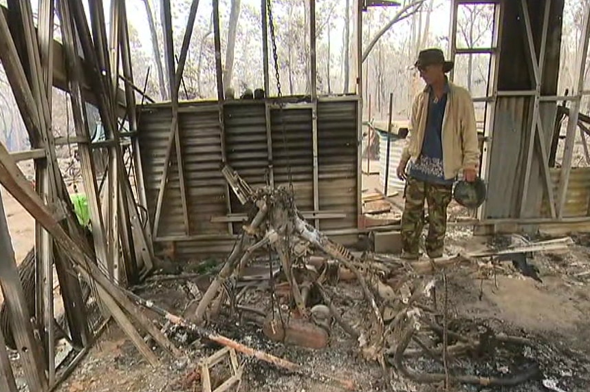 A man stands in the burnt-out shell of a building, inspecting the damage.