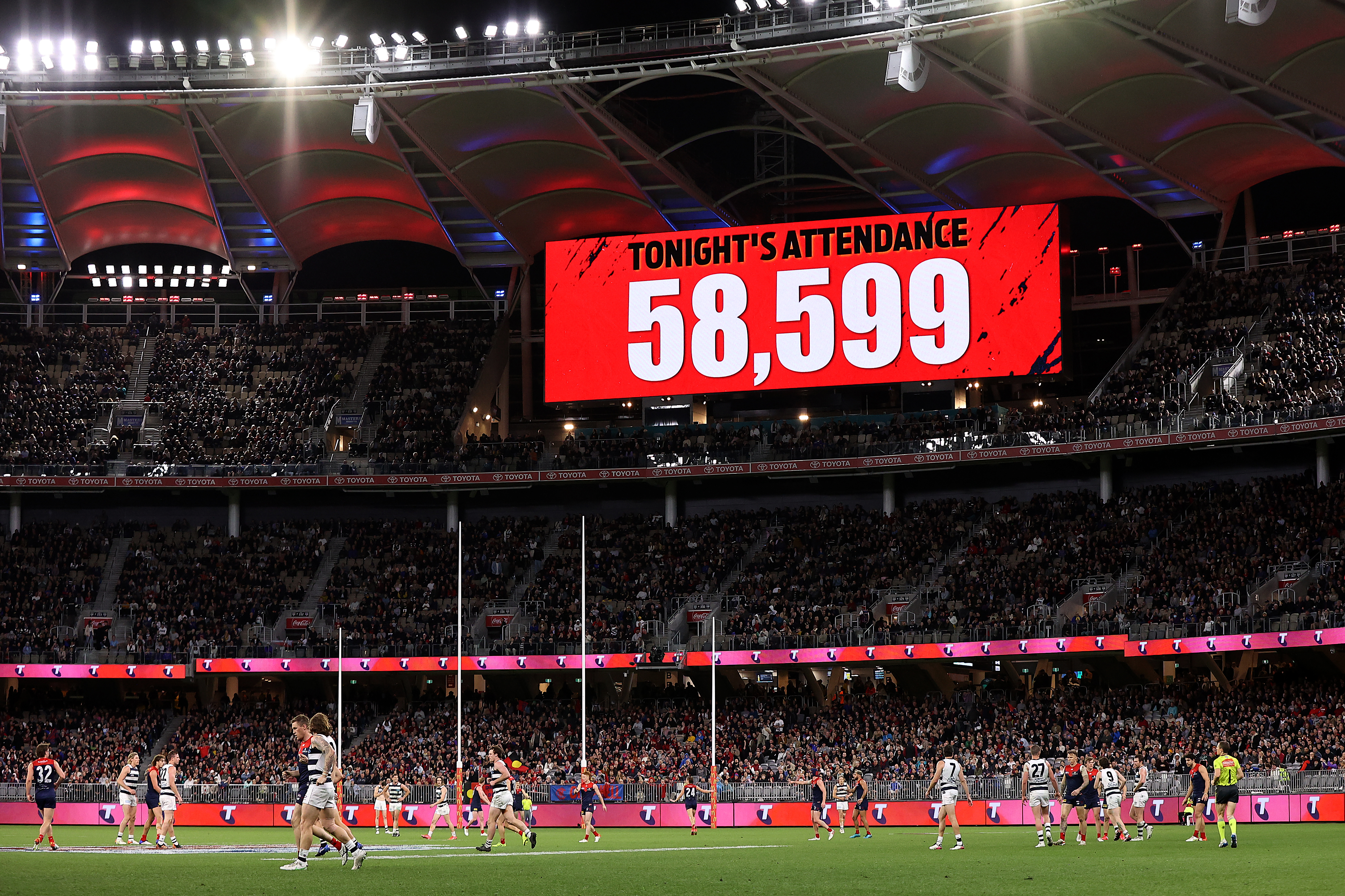 A big screen lit up in red shows the words: Tonight's attendance 58,599 at Perth Stadium during an AFL game. 