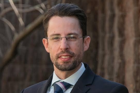 A man in glasses wearing a suit outdoors.