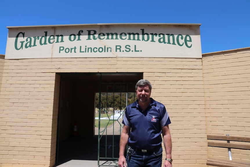 Gary Clough stands in front of a brick archway with a sign that reads Garden of Remembrance Port Lincoln RSL.