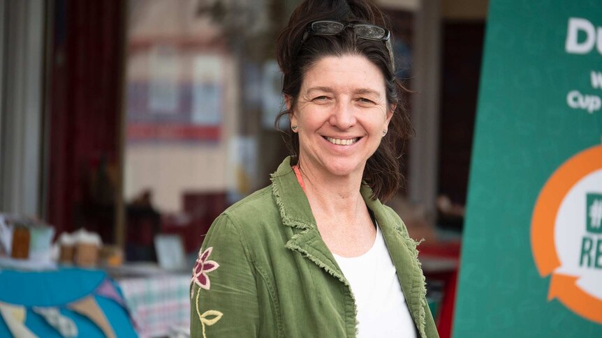 A woman in a green jacket stands next to a pull-up banner in front of a stand selling reusable products.