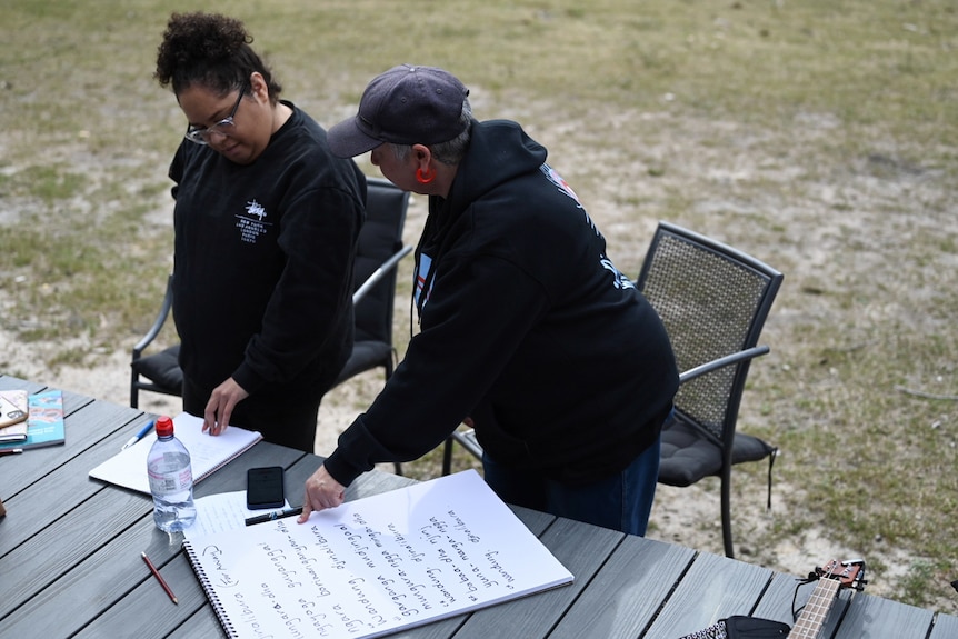 High angle shot of two women writing lyrics on a large sheet of paper.