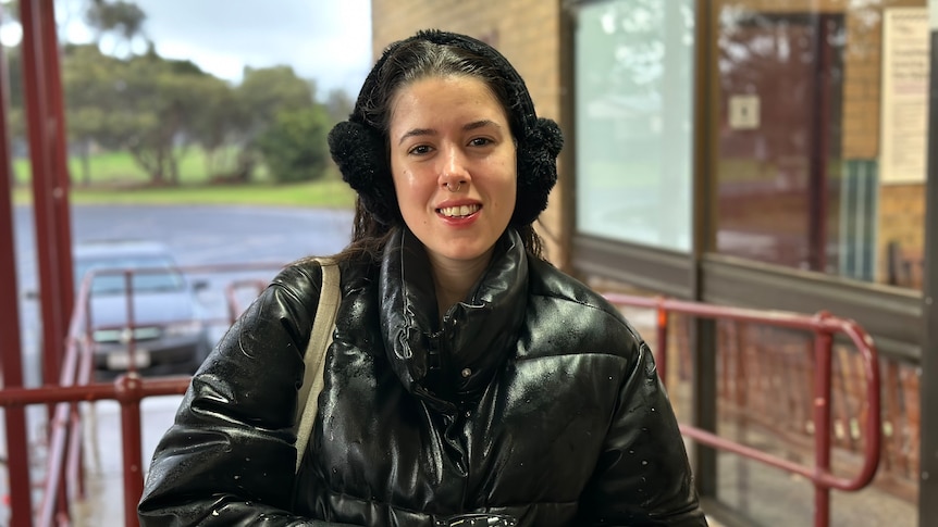 a young woman with a black jacket and black earmuffs holding a takeaway drink.