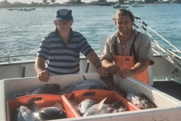 Two men behind a container full of fish.