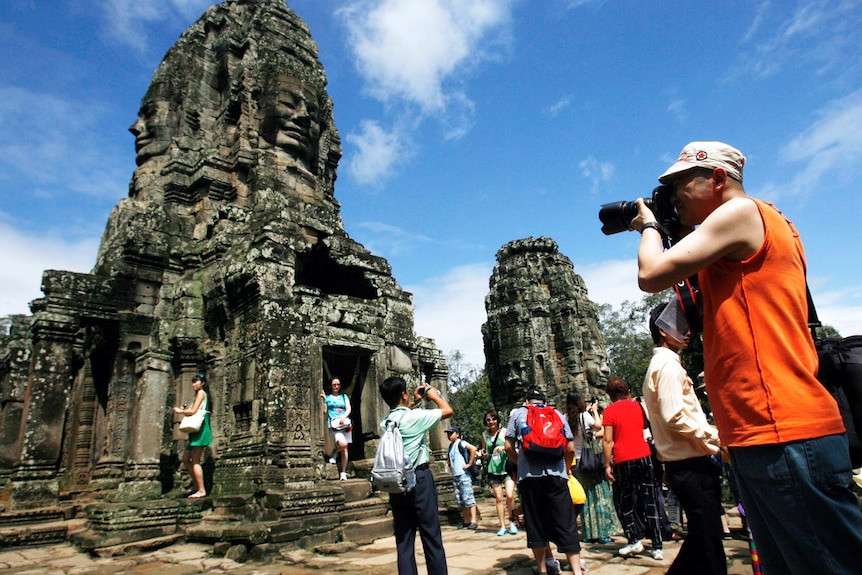 Tourists take photographs during a tour of the Bayon Temple, part of the Angkor temple complex