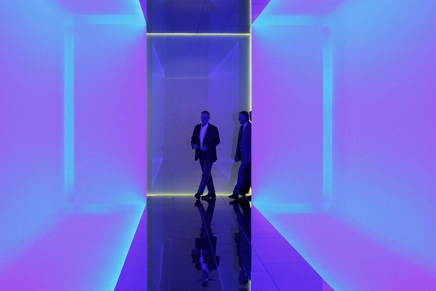 A man rounds a corner into a neon blue and purple corridor