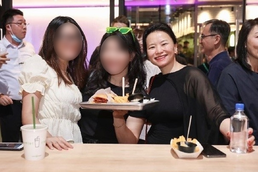 A screenshot of a post on WeChat shows three women, two have their faces blurred, posing for a photo and holding up a burger.
